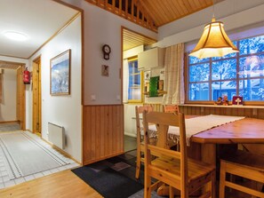Un intérieur en bois comprenant une table à manger, des chaises, un luminaire suspendu et une fenêtre donnant sur des arbres.