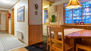 A cozy room with a wooden dining table, chairs, a hanging light fixture, a window with a view of trees, and a door leading to another room. - Korpipalo (ent. yllästunnelma 2 b 7) by Interhome (Ylläsjärvi)