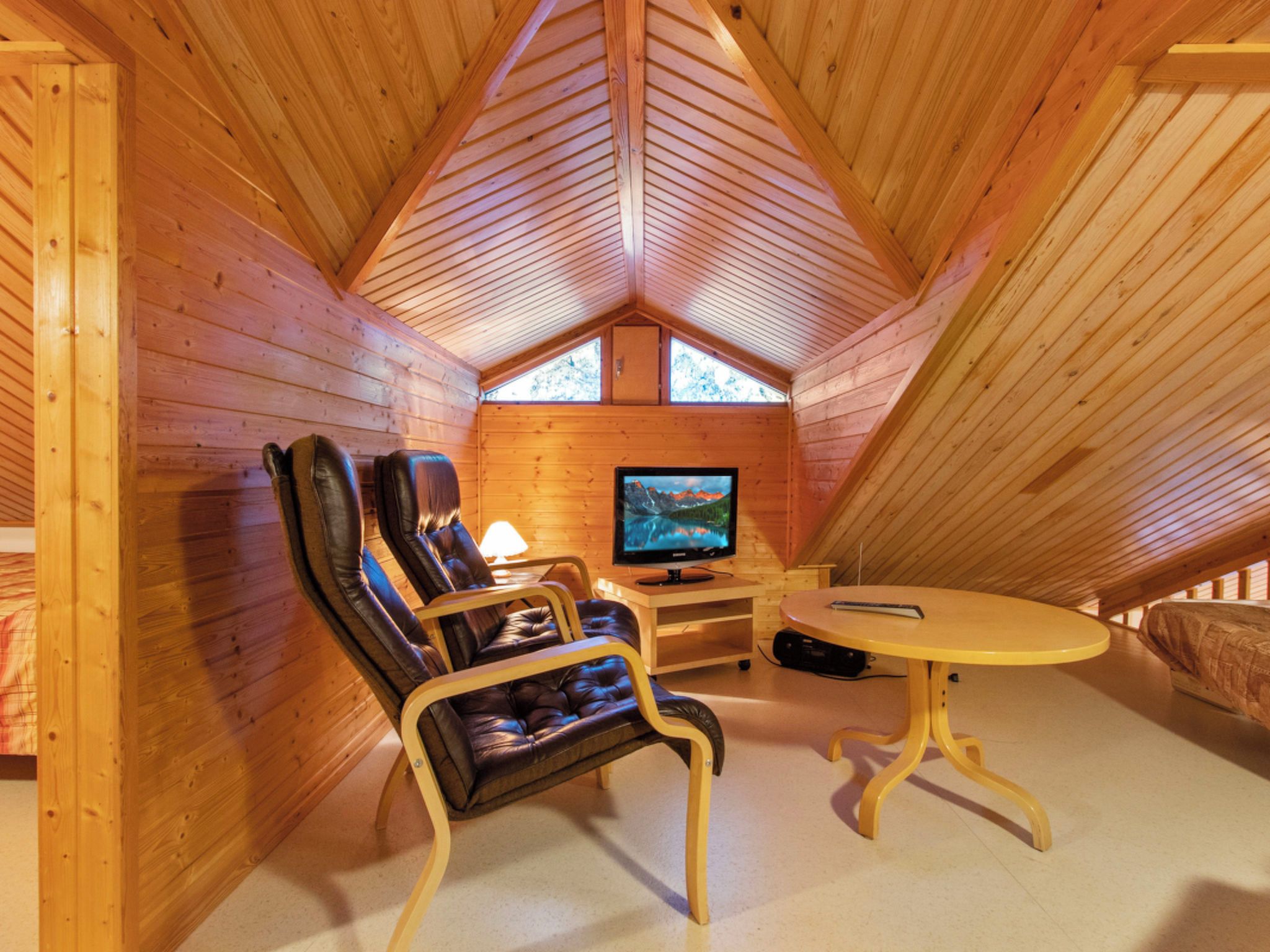 Una camera mansardata accogliente con pareti in legno, una televisione, una poltrona in pelle e un tavolino.