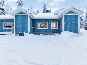 Un bâtiment bleu avec un toit enneigé, une fenêtre visible avec une lampe et une enseigne sur laquelle on peut lire « Korpivalo ».