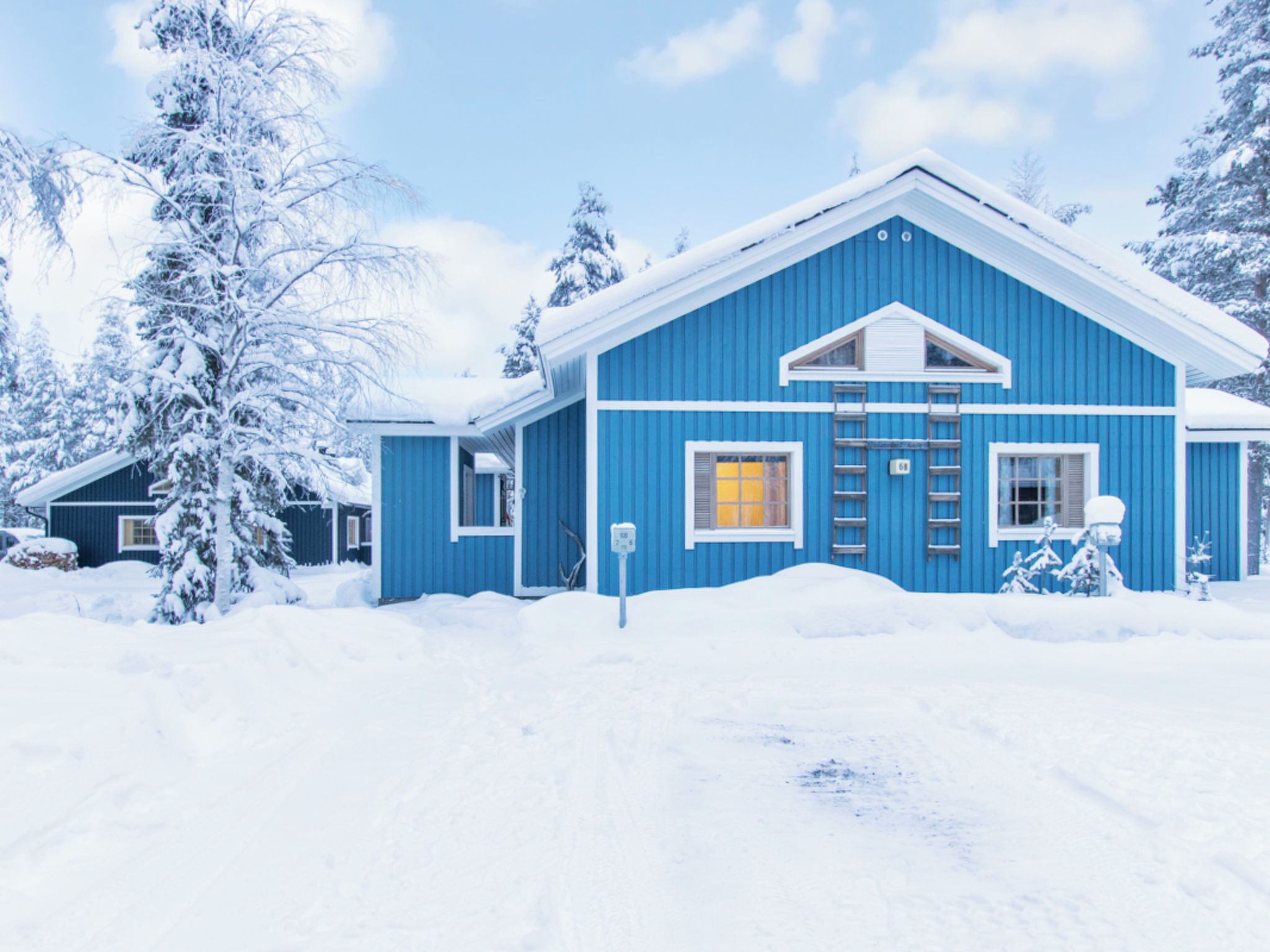 A blue house with a yellow window, surrounded by snow-covered trees.