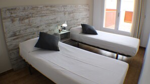 Deux lits simples avec du linge de lit blanc et des oreillers foncés, une table de chevet avec une lampe et une tête de lit en bois.