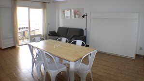 Un coin repas avec une table en bois et des chaises blanches, un canapé gris et une lampe sur pied.