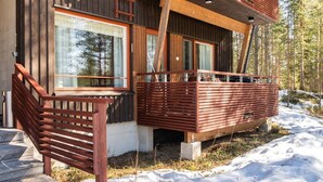 A modern wooden cabin with a balcony, large windows, and a staircase leading to the entrance.