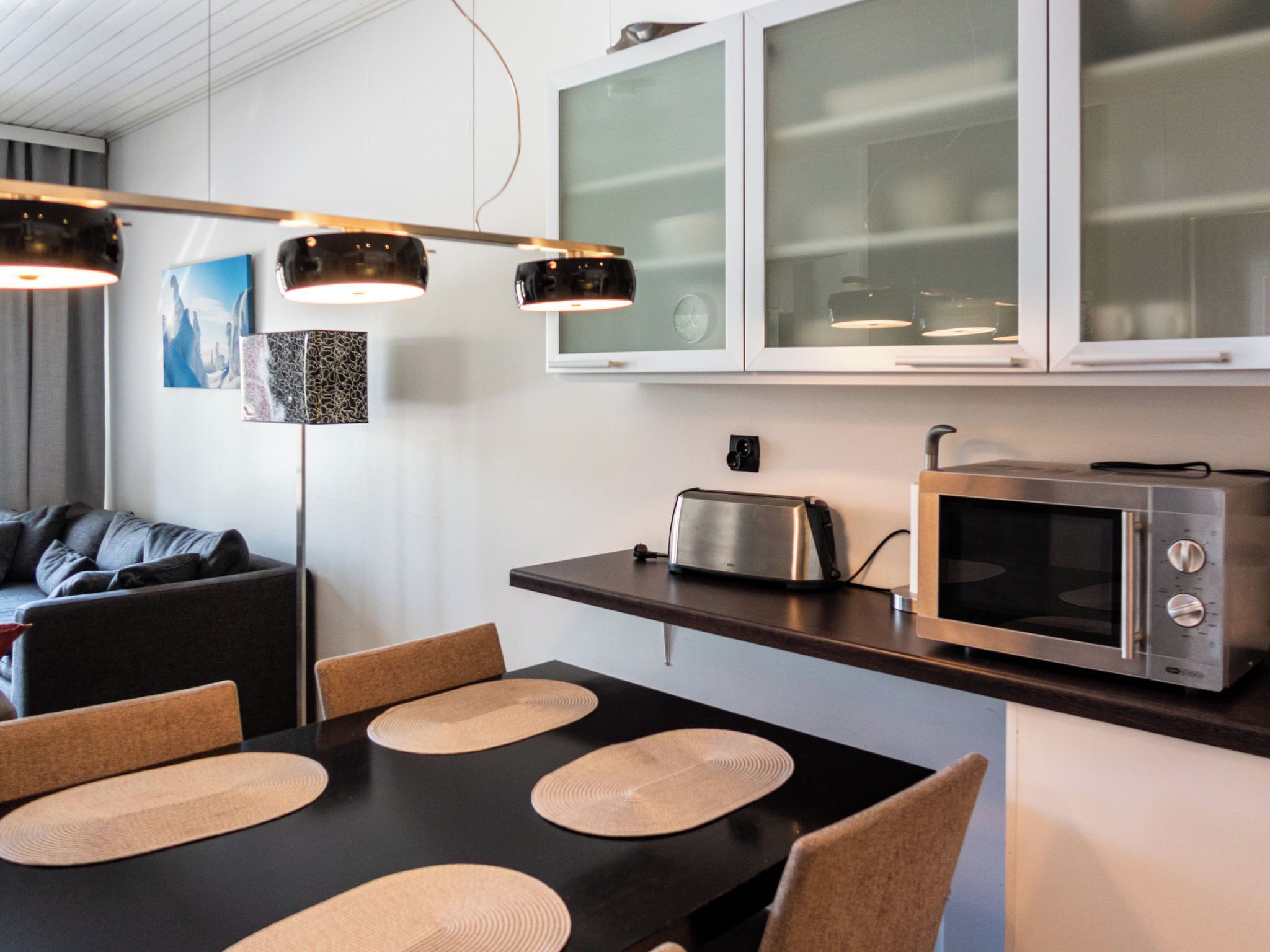 A modern kitchen with a dining table, chairs, a toaster, a microwave, and pendant lights.