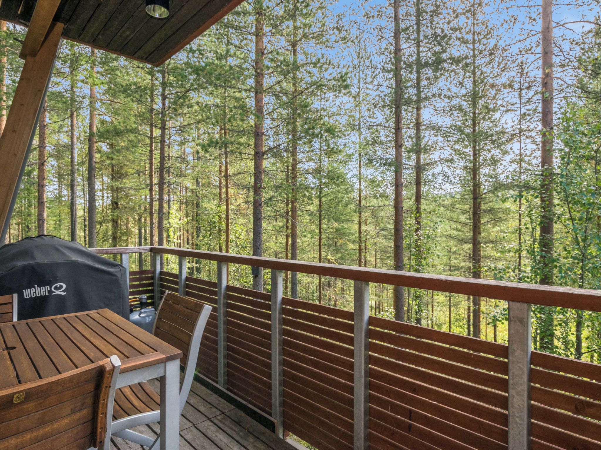 An outdoor deck with a table and chairs, overlooking a forest.