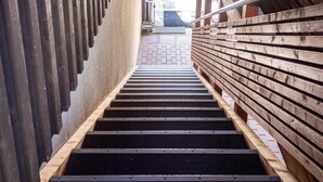 A narrow stairway with wooden steps and metal railings, leading upwards.