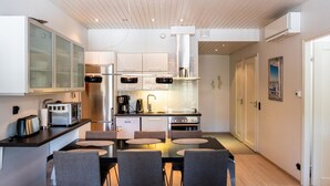 A modern kitchen with white cabinets, a dining area with a table and chairs, and a view of the city through a door.