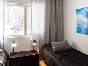 Ein Schlafzimmer mit einem Bett, einem Nachttisch, einer Lampe, einem Fenster mit Vorhängen und einem Gemälde an der Wand.