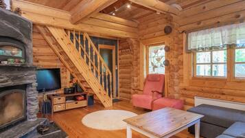Ein rustikales Blockhaus-Interieur mit Kamin, Fernseher, einer Treppe und einer gemütlichen Sitzecke.