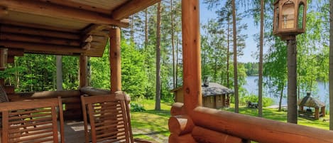 A wooden deck with a table and chairs, overlooking a lake with cabins and a gazebo.