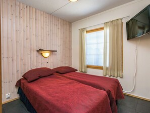 A room with two beds, a wall-mounted TV, a window with curtains, and a wooden wall. - Rukatonttu d21 by Interhome (Kuusamo)