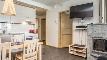 A modern kitchen with white cabinets, a dining table with chairs, a flat-screen TV mounted on the wall, and a fireplace.