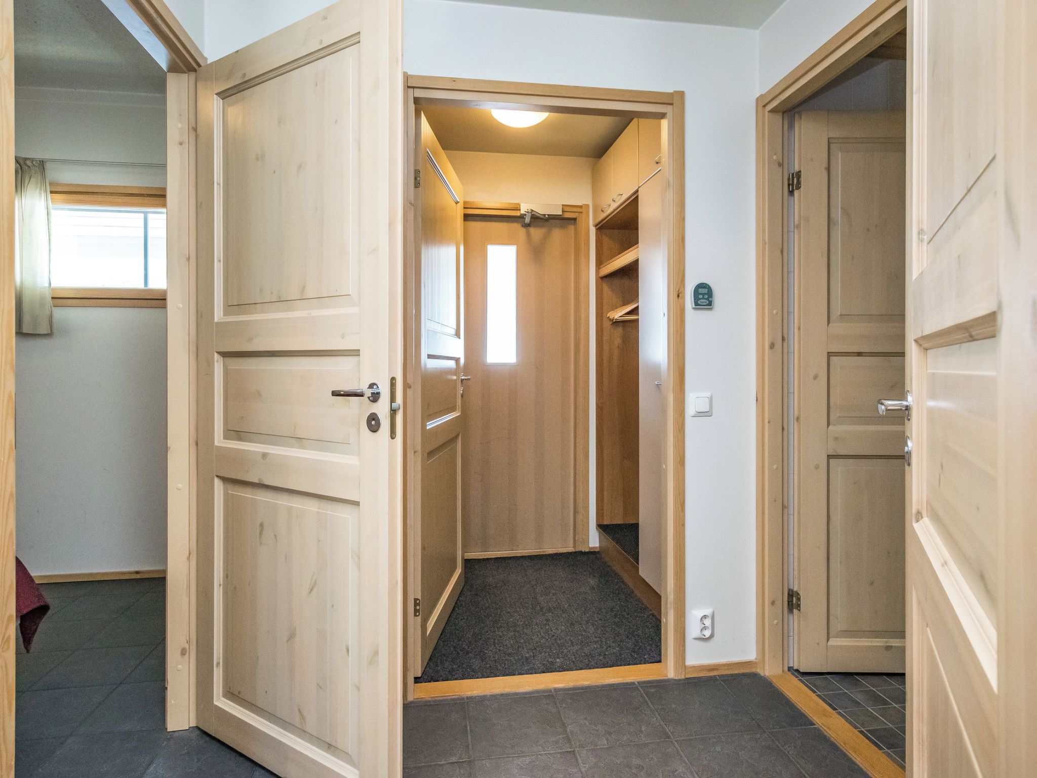 Un couloir avec des portes en bois, un sol recouvert de moquette et une petite fenêtre.