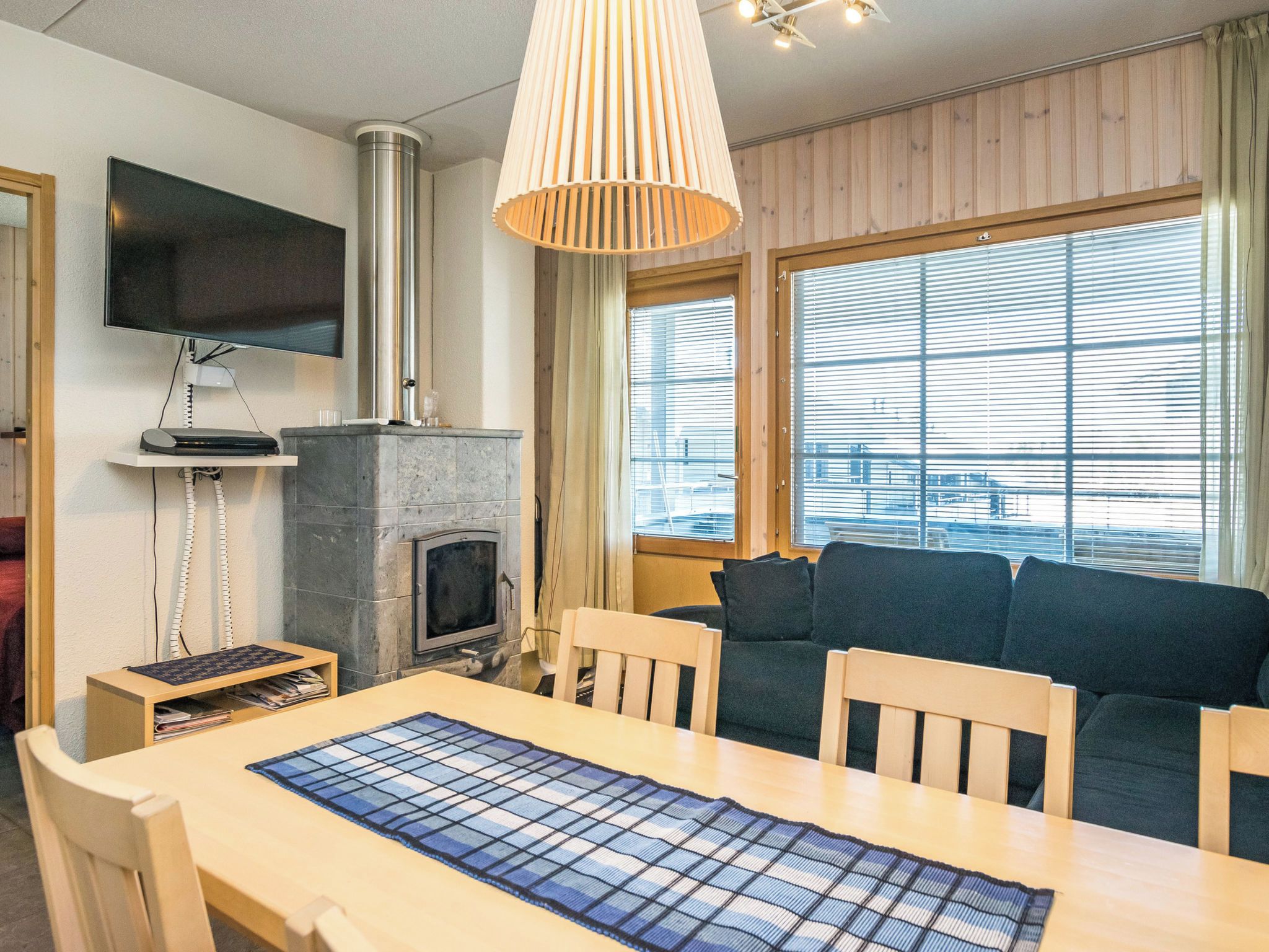 A room with a fireplace, a television mounted on the wall, a sofa, and a dining table with chairs.