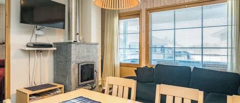 A room with a fireplace, a television mounted on the wall, a sofa, and a dining table with chairs.