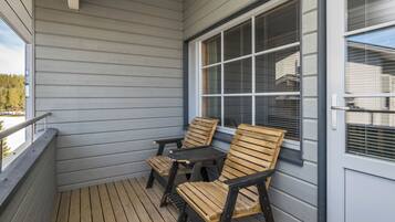 A covered porch with wooden flooring, two wooden chairs, a small table, and a window with blinds.