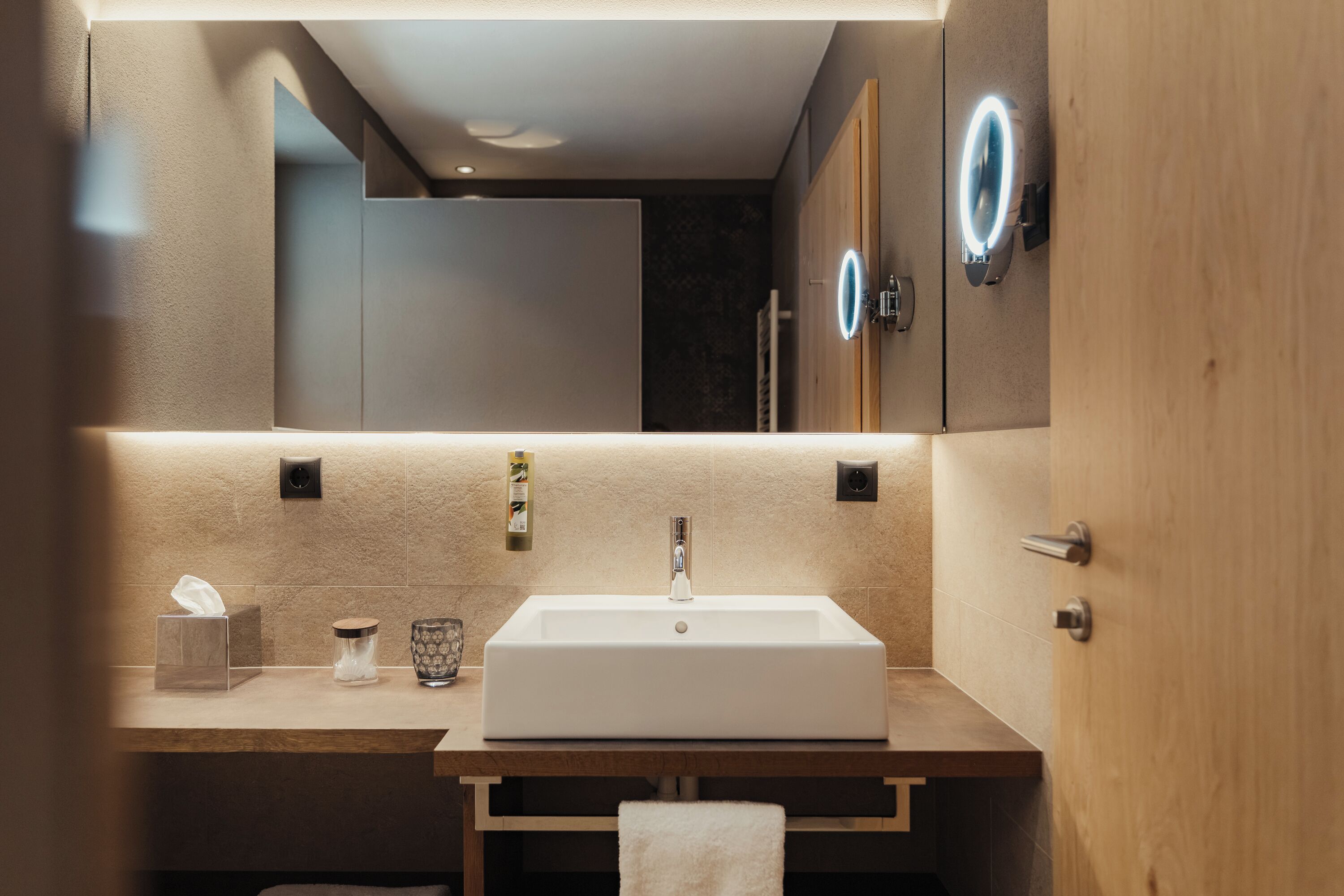 A modern bathroom with a large mirror, a rectangular sink, and a wooden vanity.