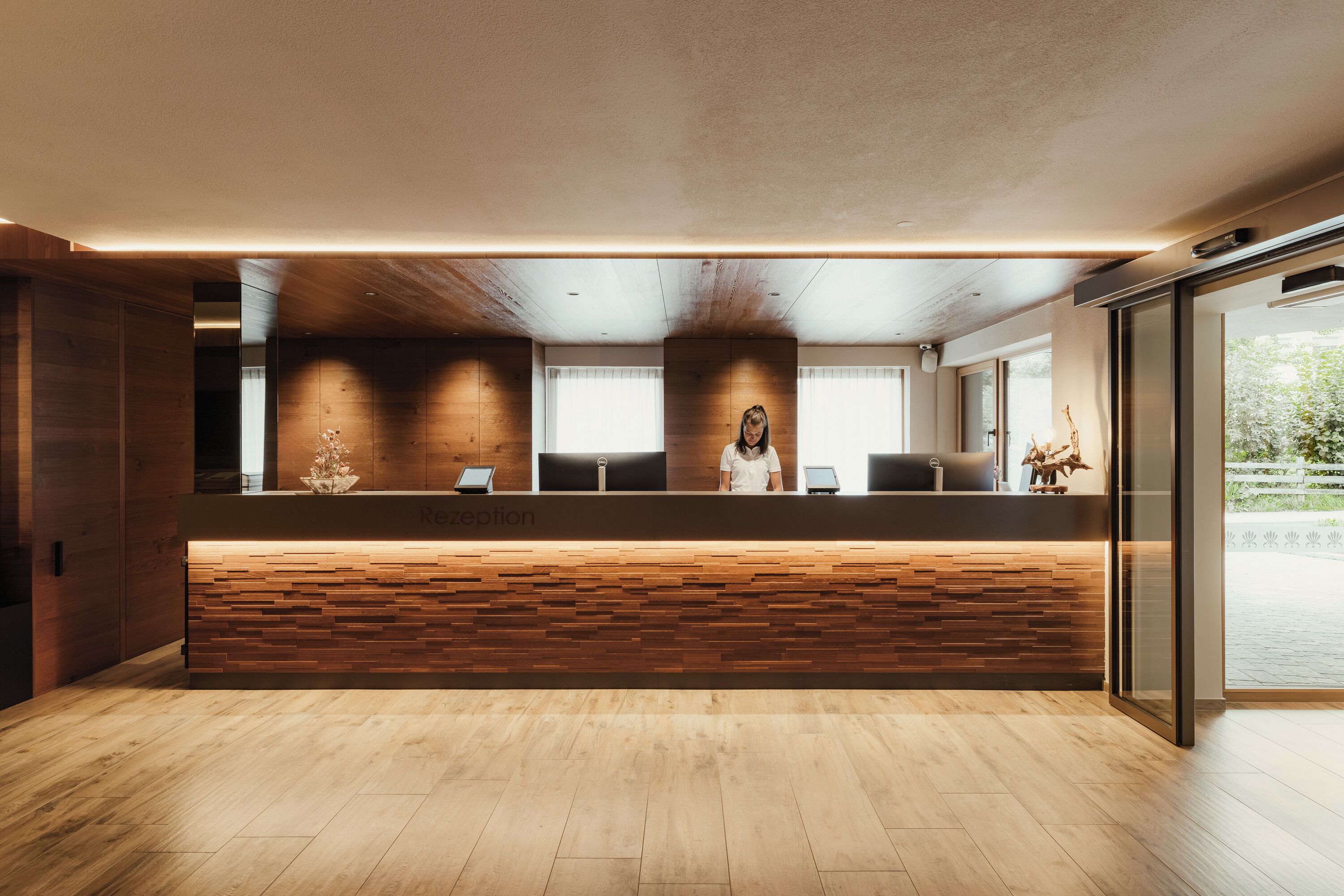 A reception area with a wooden reception desk, a glass door leading outside, and a view of the outdoors.