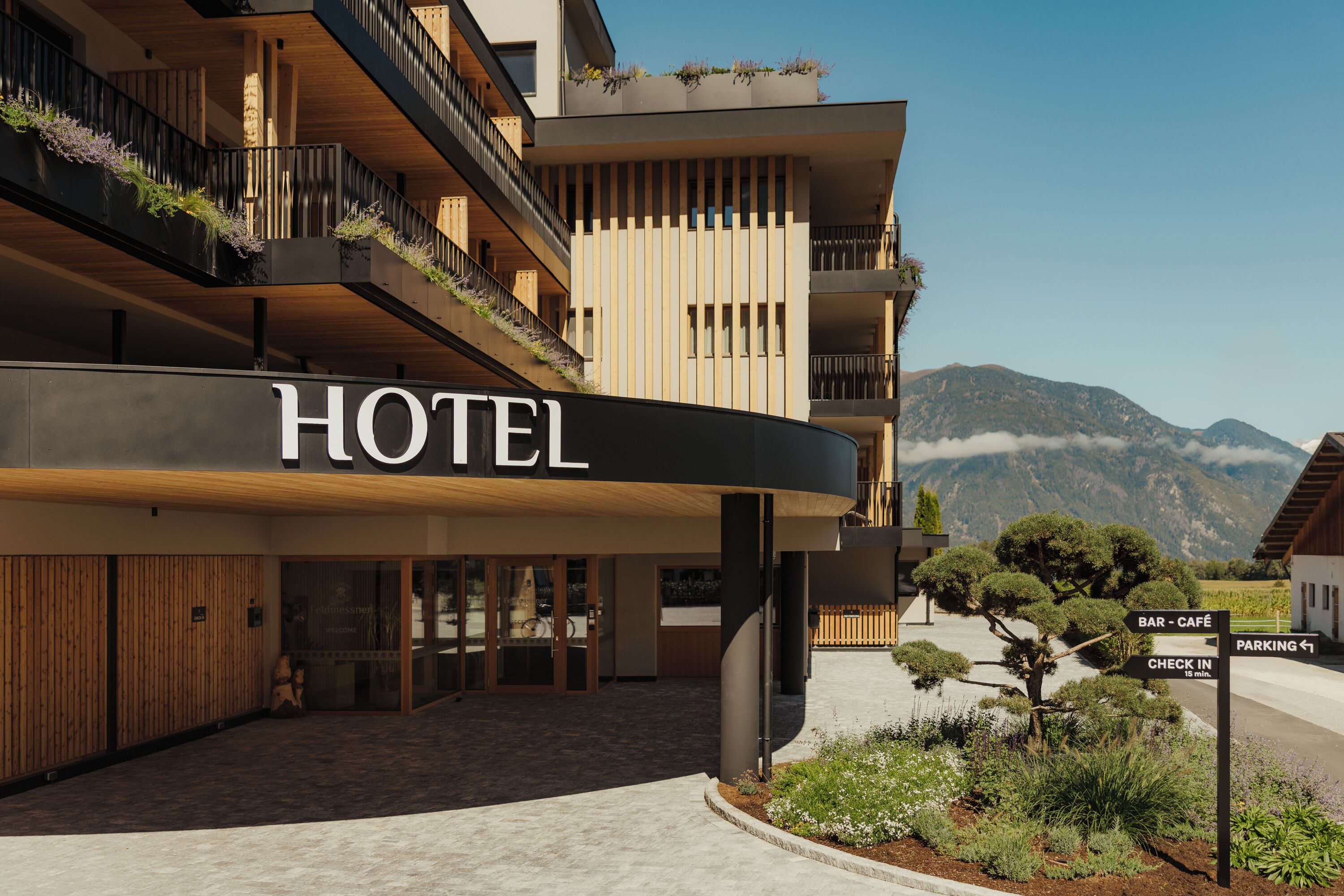 Un hôtel avec une enseigne bien visible indiquant « HÔTEL », un espace d’accueil et une vue sur les montagnes en arrière-plan.