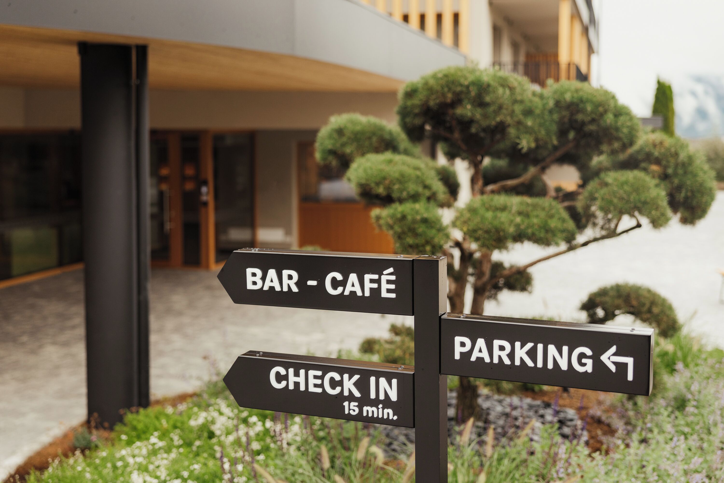 A directional sign with arrows pointing to a bar-café and parking, and a check-in sign indicating a 15-minute wait.