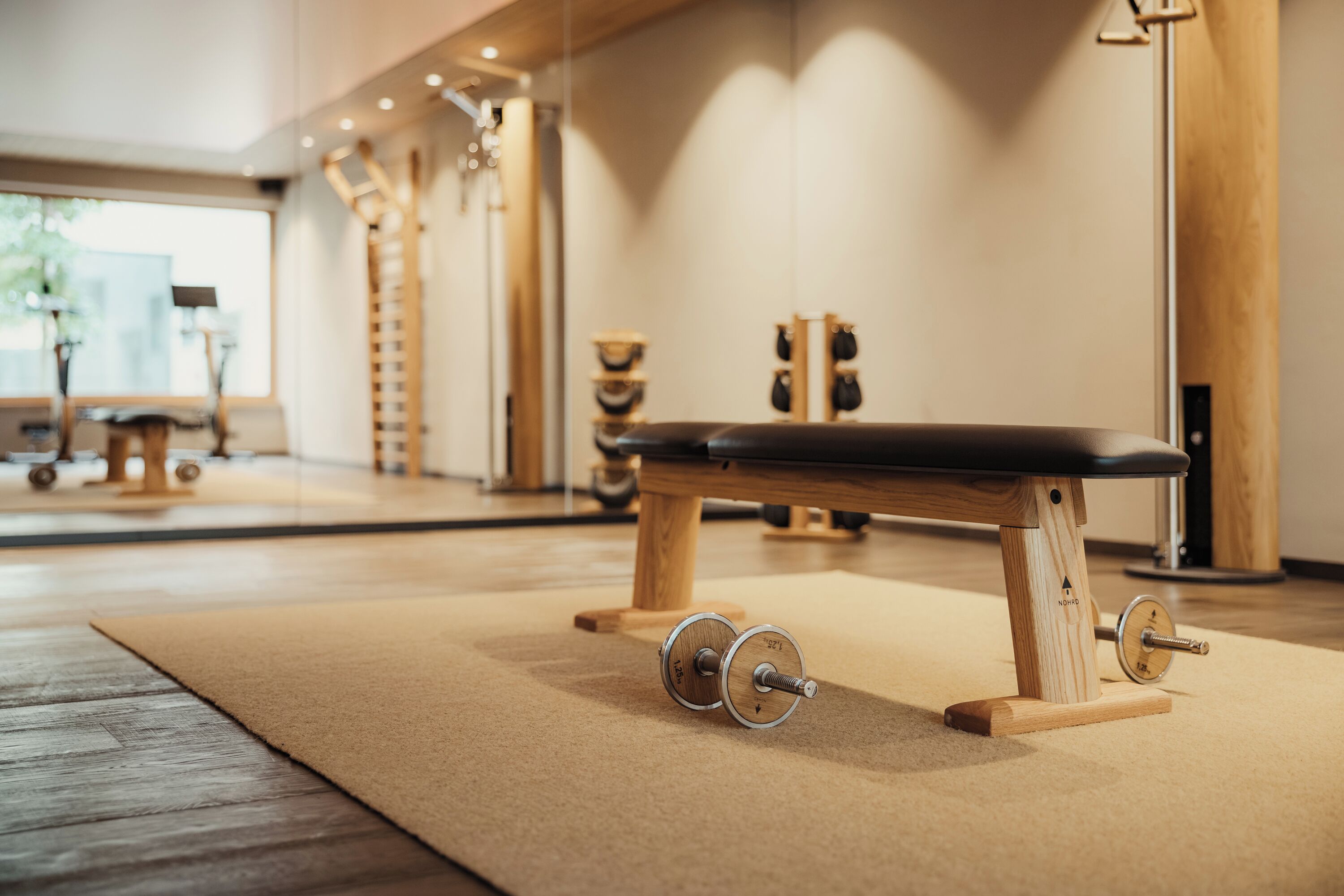 A gym with a wooden bench, weight plates, and a mirror.