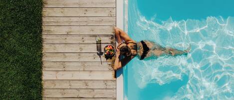 A wooden deck adjacent to a swimming pool with clear blue water.