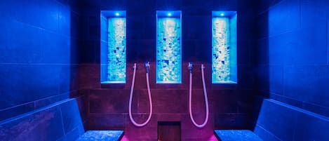 A spa room with three vertical windows, a bench, and two showerheads.