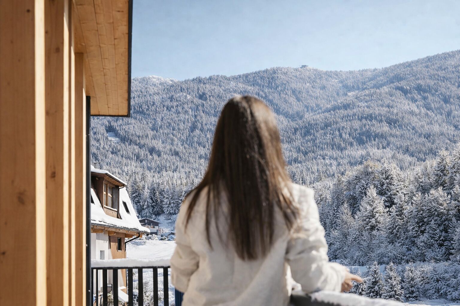 A person sitting on a balcony overlooking a snowy mountain landscape.