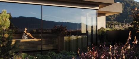 Un bâtiment moderne doté de grandes fenêtres en verre, d’une terrasse en bois et d’un jardin agrémenté de fleurs violettes.