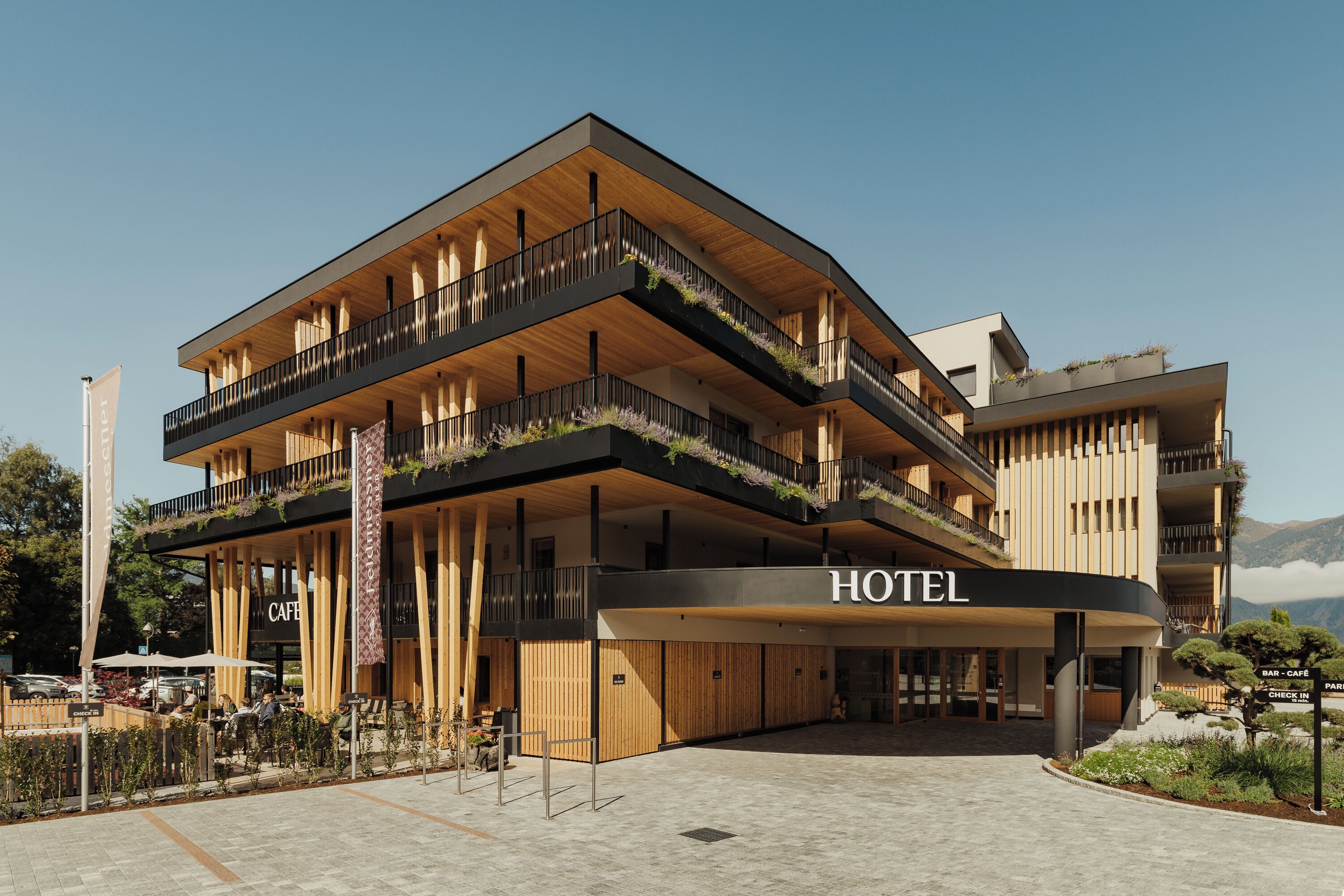 A hotel with a modern design, featuring a check-in area, a cafe, and outdoor seating.