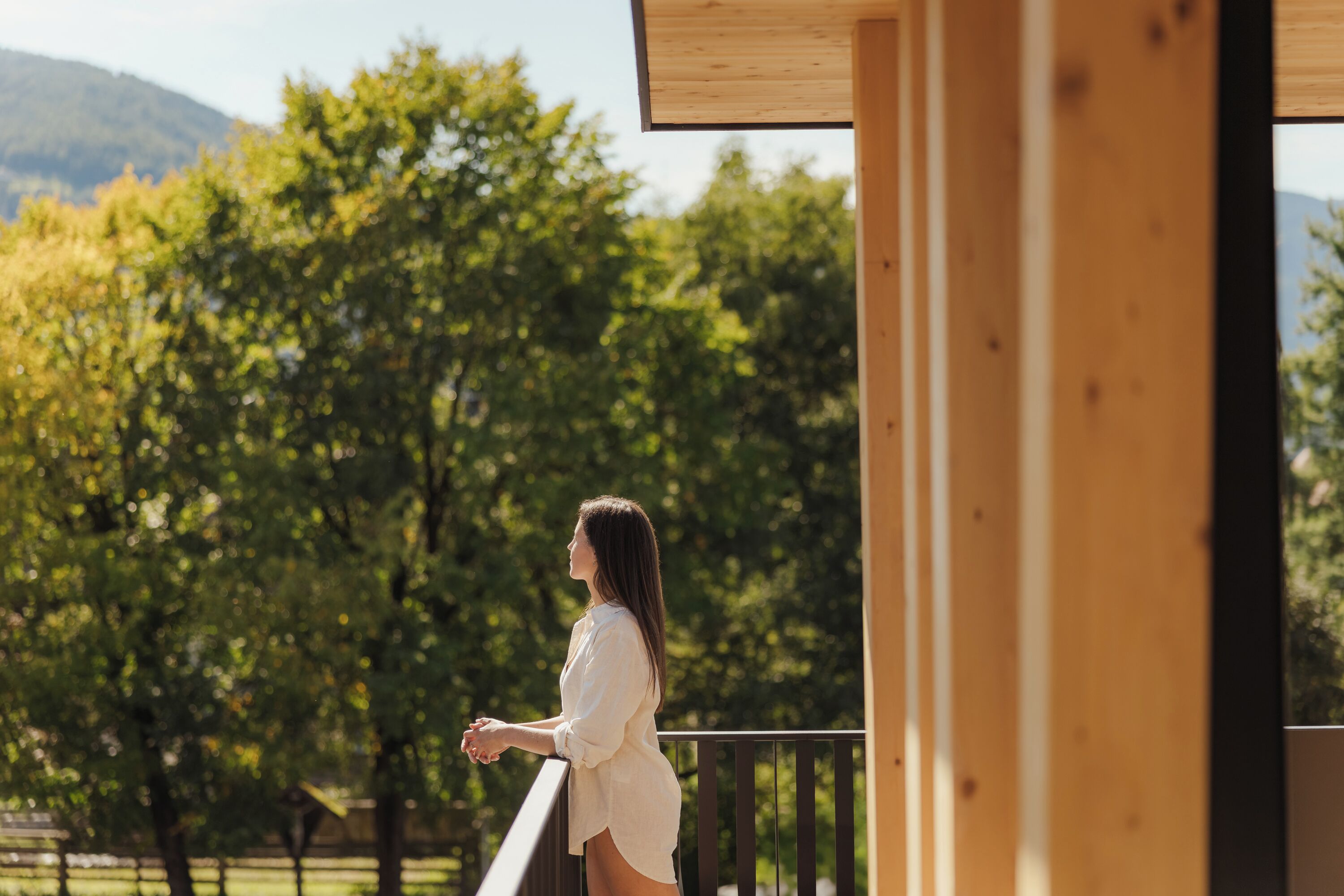 Eine Person steht auf einem Balkon mit Blick auf Bäume und Berge.