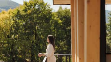 Eine Person steht auf einem Balkon mit Blick auf Bäume und Berge.