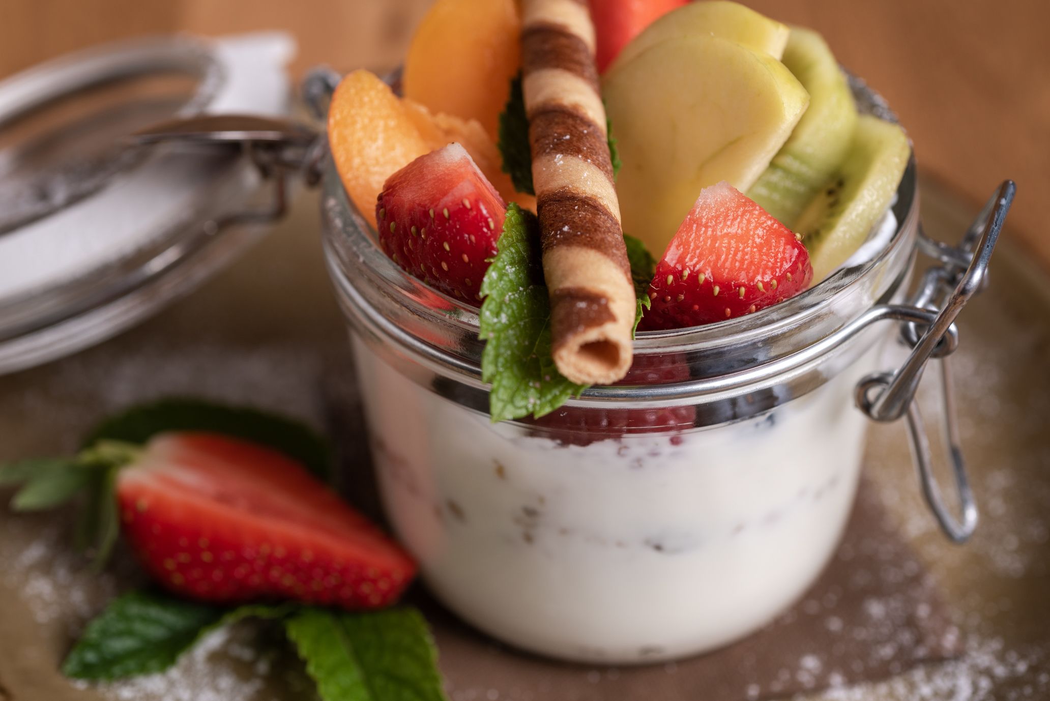 A glass jar with a metal clasp lid containing a dessert with strawberries, kiwi, and a wafer.