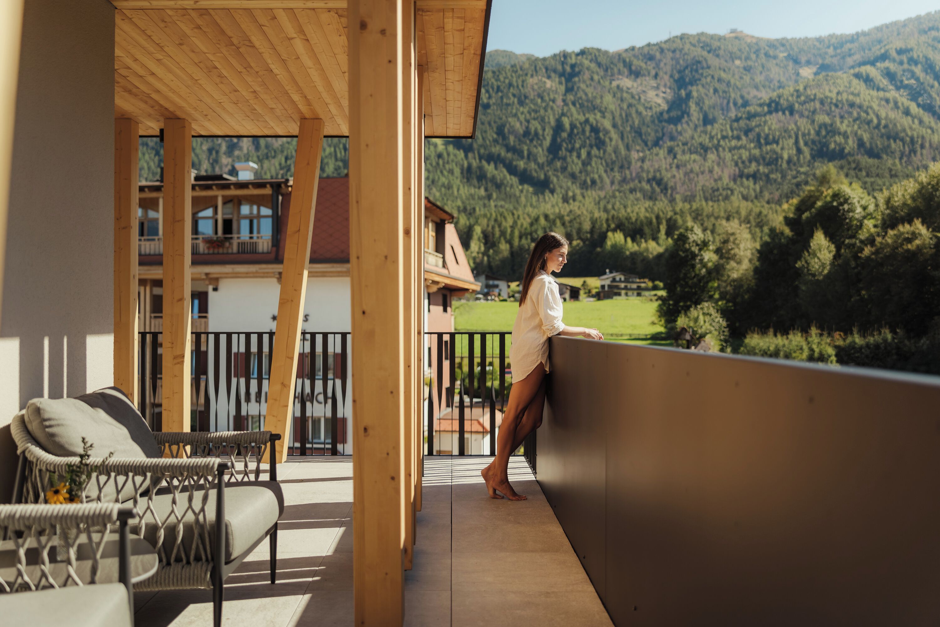 A balcony with a view of a mountainous landscape, wooden beams, and a wicker chair.