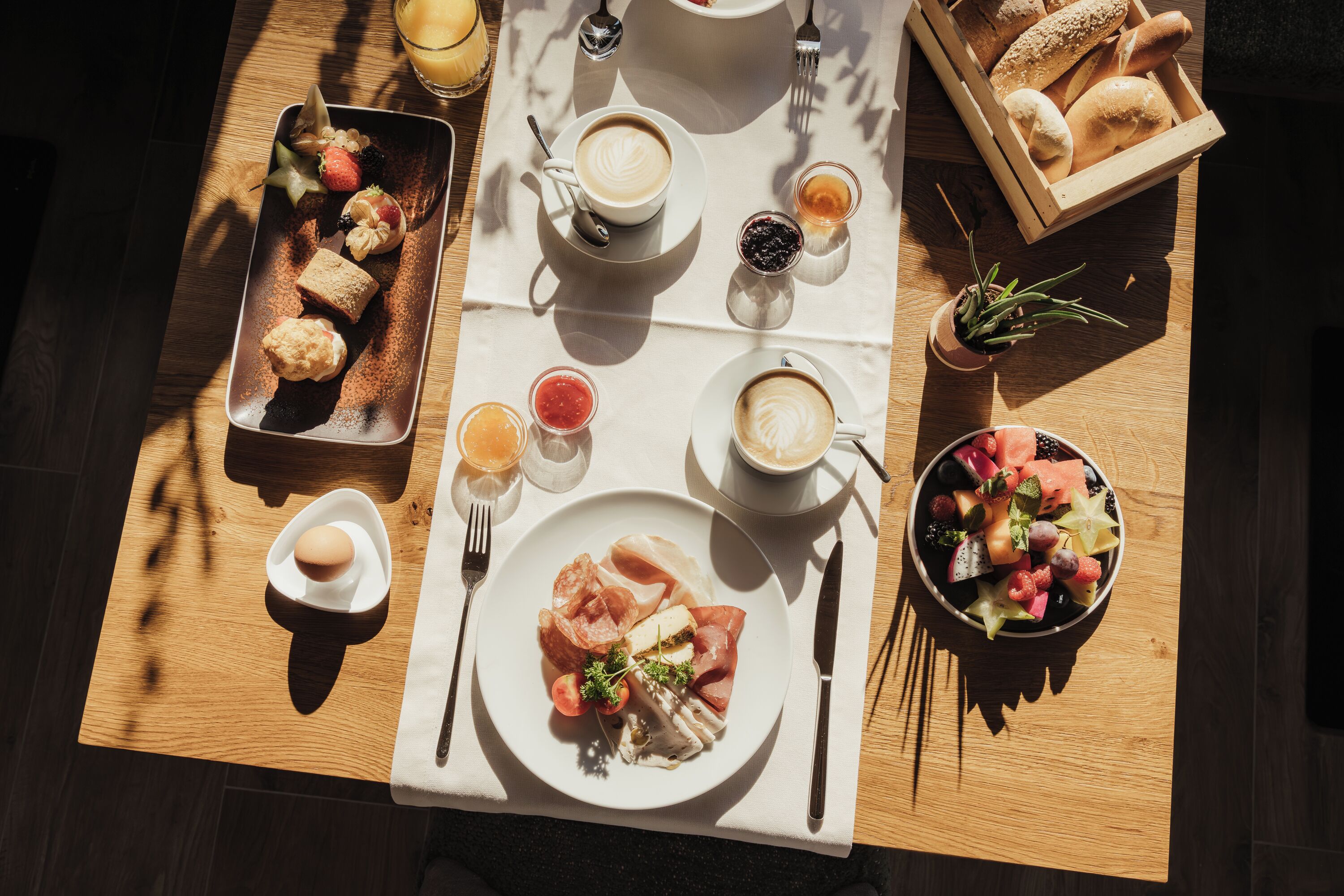 Una mesa de desayuno con cruasanes, café, fruta y bollería.
