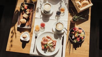 Una mesa de desayuno con cruasanes, café, fruta y bollería.