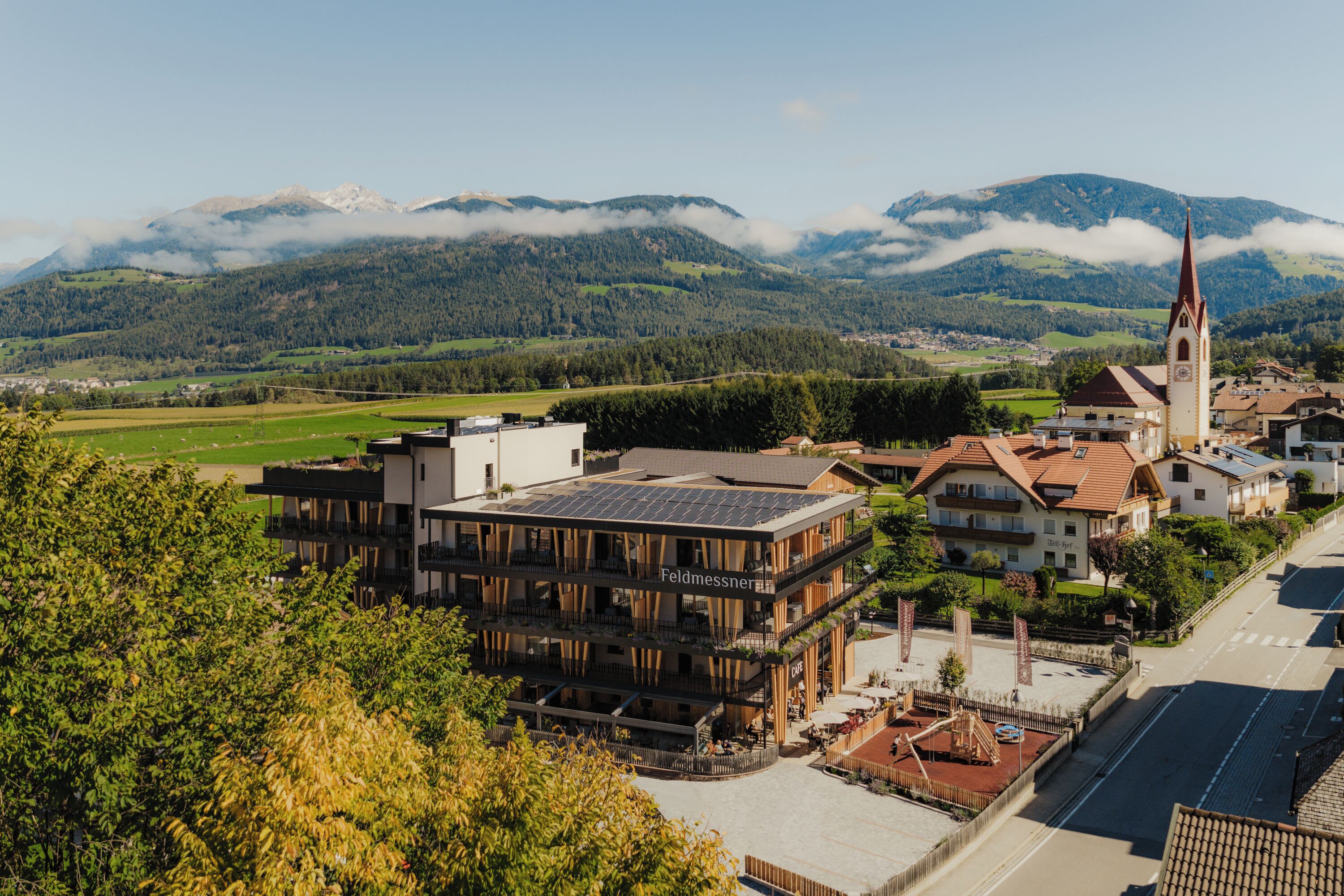A hotel with a modern design, a church nearby, and a mountainous backdrop.