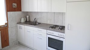 Een keuken met witte kastjes, een roestvrijstalen spoelbak, een fornuis en een kleine oven.