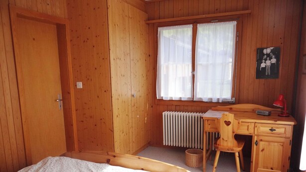 Een kamer met houten vloer, voorzien van een bed, bureau, stoel en radiator.