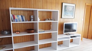 Een witte wandplank met boeken, decoratieve objecten en een televisie in een kamer met houten lambrisering.