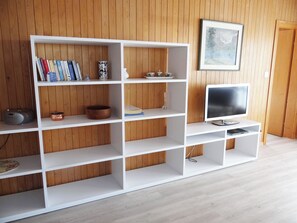 A white shelving unit with books, decorative items, and a television in a room with wooden paneling. - Valentine Appartement/Fewo 5-Bettwohnung by Interhome (Engelberg)