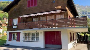 Een houten huis met twee verdiepingen, een balkon, een rode garagepoort en een berg op de achtergrond.