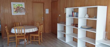 A wooden-paneled room with a dining table, chairs, a bookshelf, and a painting.