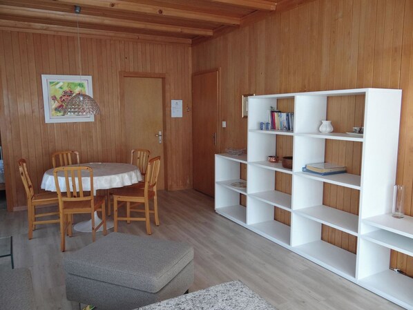A wooden-paneled room with a dining table, chairs, a bookshelf, and a painting.