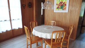 Een eetgedeelte met een ronde tafel, zes houten stoelen, een kroonluchter en een schilderij aan de muur.