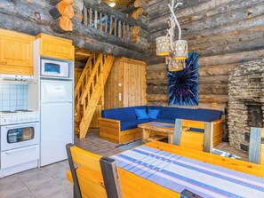Interior de uma cabana de tronco com cozinha, sala de jantar e lareira de pedra.