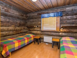 Quarto de cabana de tronco com duas camas, uma mesa pequena e uma janela com persianas.