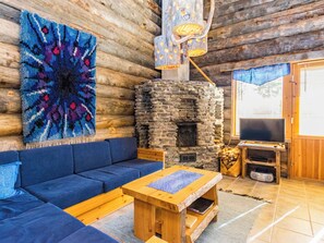 A cozy log cabin interior with a stone fireplace, blue sofa, wooden coffee table, and a large abstract painting. - Rinnekieppi 2 by Interhome (Kuusamo)