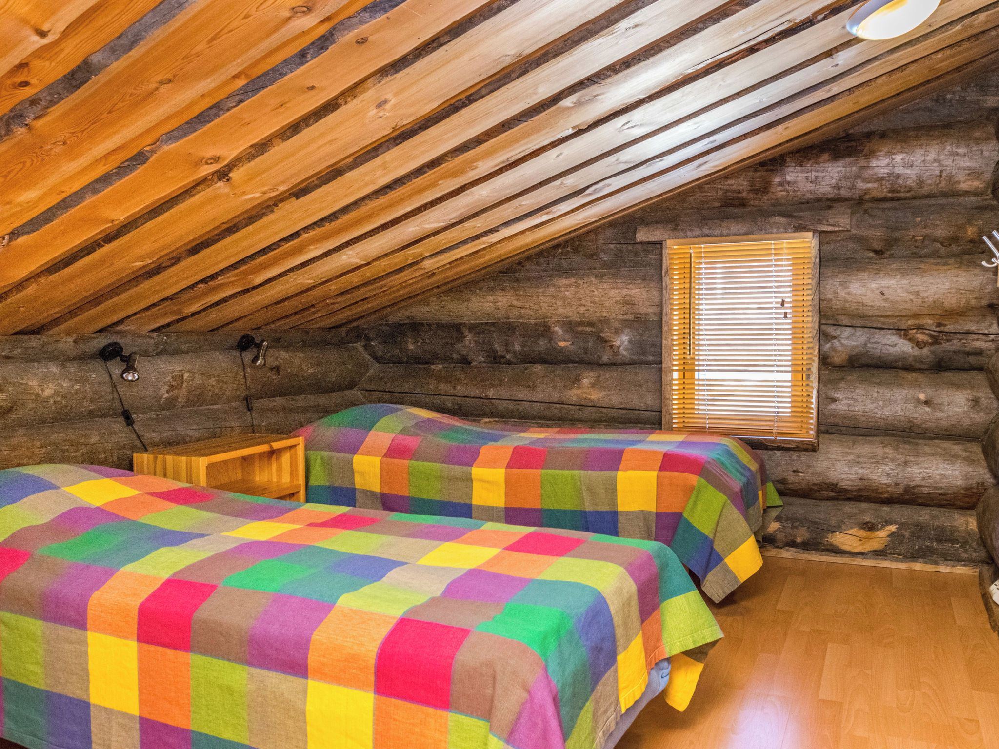 Une cabane en rondins avec deux lits, des murs en bois, un plafond en pente et une fenêtre avec des stores.